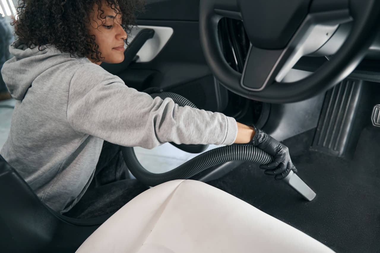 Service station worker vacuum-cleaning interior of vehicle